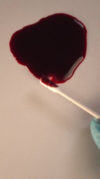 Forensic swab swabbing blood pool for crime scene investigation and lab analysis, top view slow zoom in, blue gloved hand, bottom copy space, vertical video