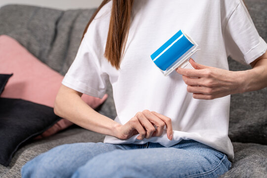 Woman refreshes white t-shirt with reusable adhesive roller, blue gel surface removing lint and dust. Concept of slow fashion mindset and extending clothing lifespan through daily garment maintenance