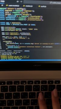Close up view of a female programmer's hands typing on a laptop keyboard, with colorful javascript code visible on the screen, showing the process of web development