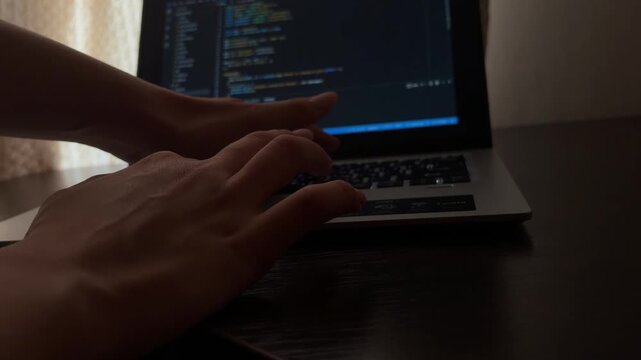 Professional programmer coding and typing on a laptop keyboard at night, focusing on software development, hacking, and cybersecurity concepts in a dark room