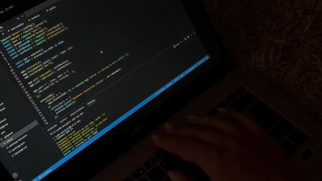 Female programmer's hands typing javascript code on a laptop keyboard in a dark room, highlighting the digital workflow of a software developer creating an application
