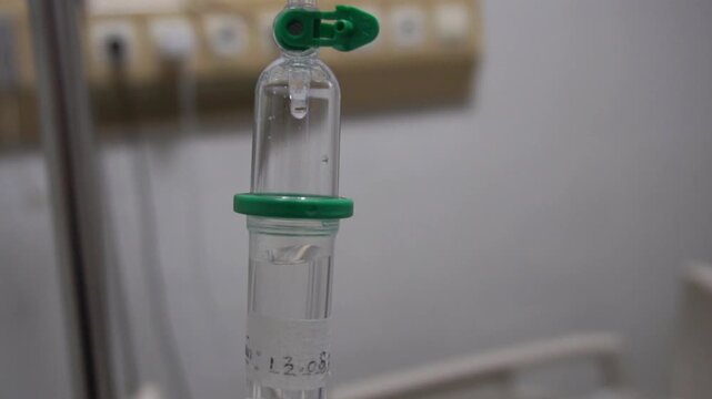 Close up intravenous drip chamber with saline solution drop in hospital room, medical iv fluid therapy equipment concept for health care and treatment.