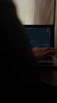 Anonymous programmer coding at night on a laptop. Dark home office environment with a professional developer typing on the computer keyboard, focusing on the screen