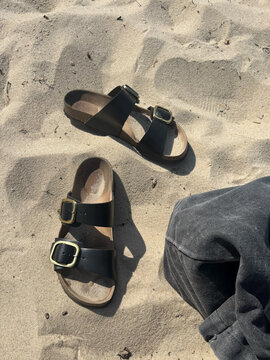 Black leather sandals left on beach sand for summer vacation relaxation and casual footwear concept