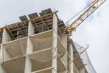 Construction continues on a tall building with a crane at work under a cloudy sky © beholdereye