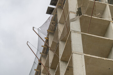 Concrete structure rises against a gray sky as construction workers prepare for the next phase of urban development © beholdereye