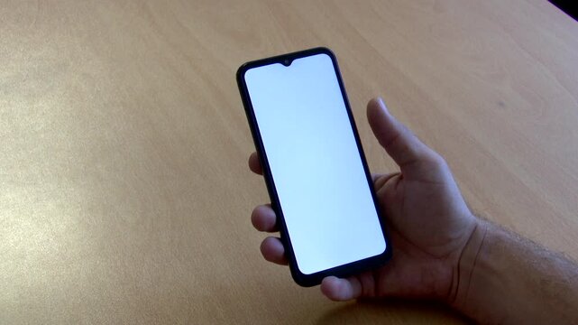 High-resolution 4K close-up video of a hand unlocking a sleek black Android smartphone resting on a wooden table, revealing a clean, solid white screen. Ideal for mobile app mockups, UI/UX screen repl