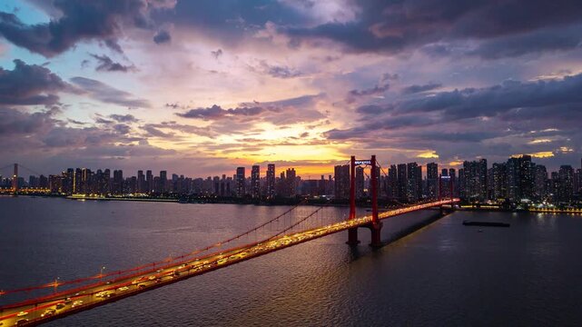 The illuminated bridge spans across the river in the city of Wuhan China during a vibrant sunset with a scenic urban skyline in the background