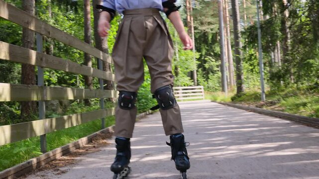 Woman keeping balance on rollerblades with one arm raised, learning to skate in a summer park. Beginner practicing technique and coordination on a park track, outdoor sport training in the forest.