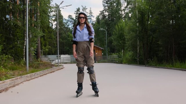 Happy woman in a helmet on rollerblades spreads her arms on a forest path, freedom and joy concept. Active summer weekend in a pine park, positive emotions and carefree mood of an adult woman.