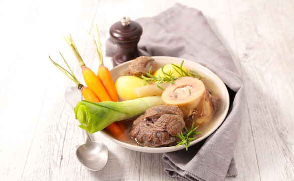 beef pot au feu stew with marrow bone leek carrots and potatoes in ceramic bowl on wooden table