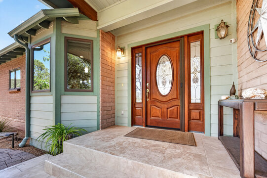 Front porch entrance with wooden double door, stained glass panels, brick siding exterior entry gate