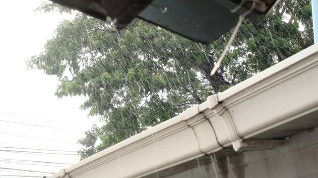 Heavy rain flows through a white gutter during a storm