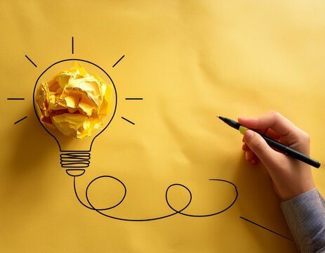 creative brainstorming concept showing a hand drawing a lightbulb connected to crumpled yellow paper representing idea generation