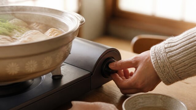 Hand turning stove knob beside steaming nabe hot pot for winter dinner
