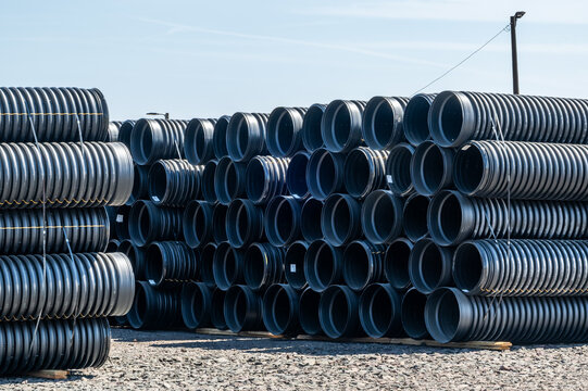 View of large black corrugated plastic drainage pipes stacked in rows at a construction supply yard in Eugene, Oregon, United States.