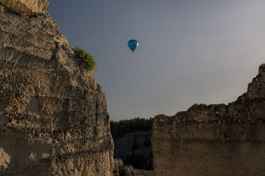 View of a hot air balloon floating in the sky between the rugged limestone canyon walls of Gravina in Puglia, Apulia, Italy.