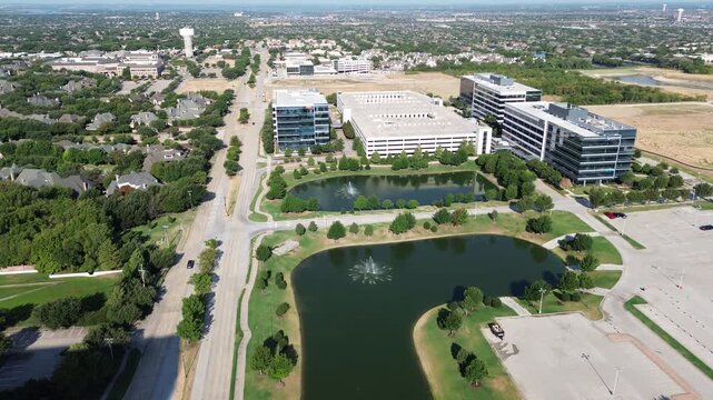 Fountain aerated lake system anchors corporate office park along North Texas Platinum Corridor. Expansive surface parking flanks multi story office blocks across flourishing Frisco, Texas