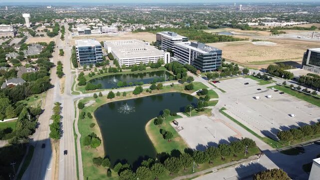 Twin fountain lakes reflect blue skies beside corporate office complex within DFW metroplex. Asphalt parking lots border commercial facilities across master planned zone in Frisco, Texas