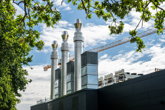 View of a modern data center facility with tall metallic exhaust pipes and cooling units under a blue sky with a construction crane in Rellingen, Schleswig-Holstein, Germany.