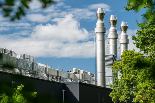 View of the modern data center facility with industrial ventilation ducts and tall metal exhaust chimneys set against a blue sky with green trees in Rellingen, Schleswig-Holstein, Germany.
