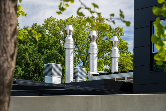 View of the metallic ventilation stacks on the roof of a modern data center building surrounded by lush green trees in Rellingen, Schleswig-Holstein, Germany.
