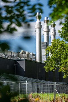 View of the modern data center facility featuring tall metallic exhaust chimneys, dark exterior walls, and surrounding green trees in Rellingen, Schleswig-Holstein, Germany.
