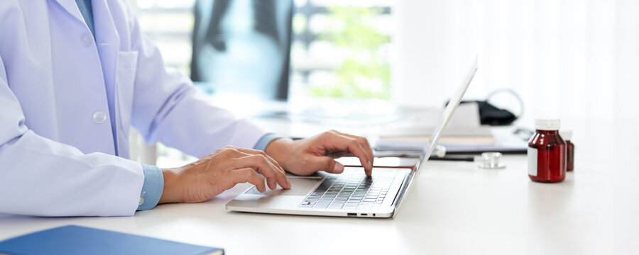 Doctor using a laptop .Physician working with technology in office, wearing a white lab coat and a stethoscope.
