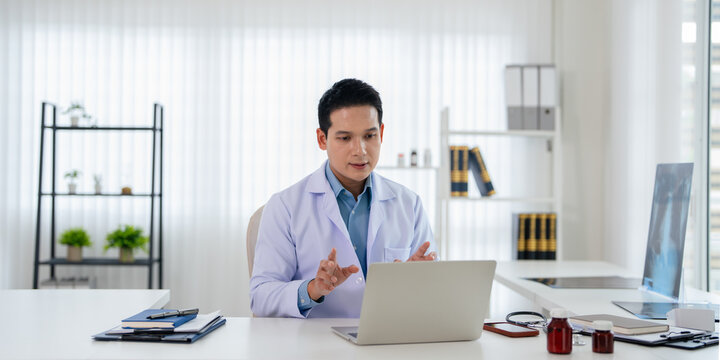 Confident asian doctor talking on video call by looking at camera from hospital with patients. concept of online counseling, medical advice and consultation.