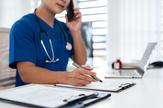 asian male doctor  reads a medical report on a clipboard while talking on the phone in a hospital  office. TeleHealth
