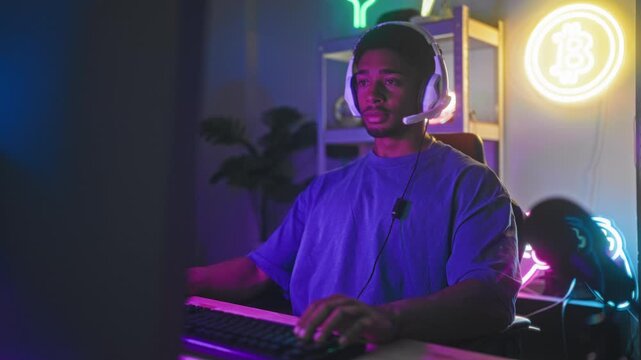 Man wearing headset, hands on keyboard and speaking into mic in a neon bitcoin gaming studio with shelves and plant; focused gameplay session.