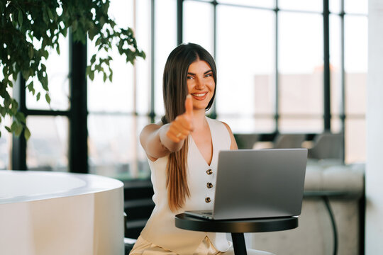 Professional woman smiling and giving a thumbs up at a modern laptop