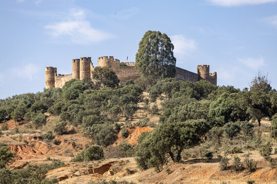 View of the medieval Castle of Monsaraz perched on a hilltop surrounded by lush trees and shrubbery under a clear blue sky in Monsaraz, Evora District, Portugal.
