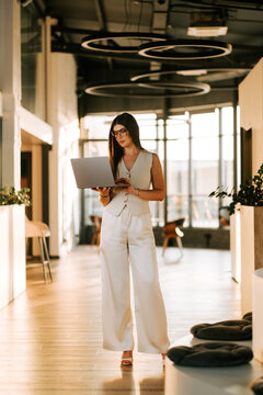 Professional woman working on a laptop while standing in a modern office during the late afternoon