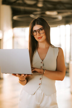 Professional woman using a silver laptop while standing in a bright modern office during the day