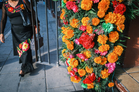 View of a woman in a traditional black dress walking past a vibrant floral arrangement made of orange marigolds for Dia de los Muertos in Oaxaca, Oaxaca, Mexico.