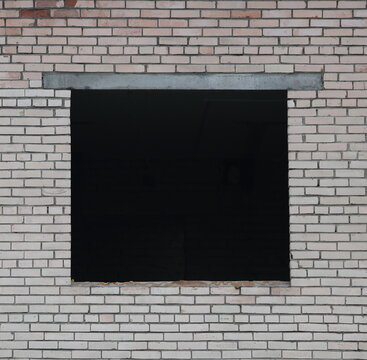 A square window opening without a window frame in a wall made of white brick
