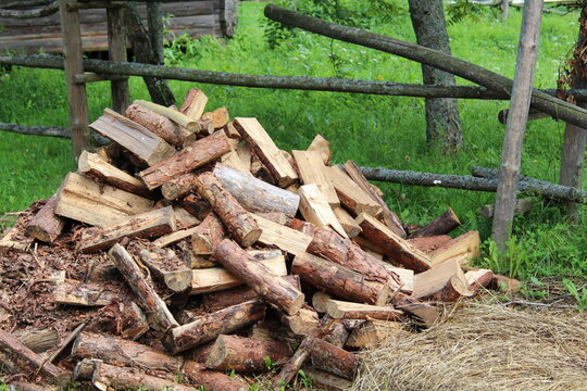 Neatly stacked firewood logs with bark and sawdust near a rustic wooden fence.