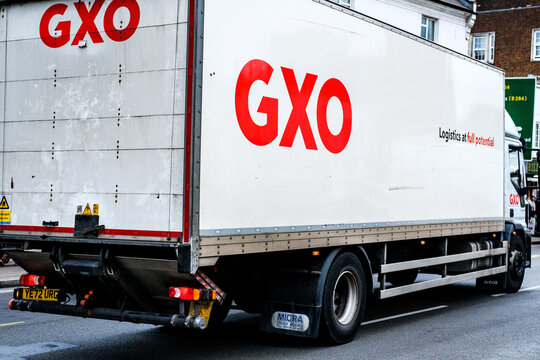 Close-Up Of A White Branded GXO Logistics Rigid Lorry Driving Along A Town Centre High Street
