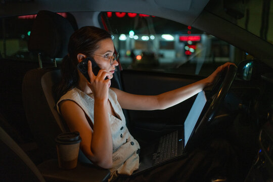 Businesswoman talking on phone and working late hours from a parked car