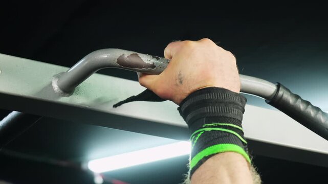 Strong man athlete grips sturdy pull-up bar in modern gym before beginning upper-body workout. Sportsman prepares to perform controlled pull-ups