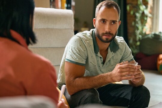Serious male client listening to psychologist during consultation. Concept of psychoeducation, treatment guidance, trust, and informed participation in mental healthcare.