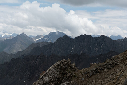 View of the rugged peaks of the Tian Shan mountains with rocky slopes, patches of snow, and dramatic clouds over the landscape in Ak-Su, Issyk-Kul Region, Kyrgyzstan.