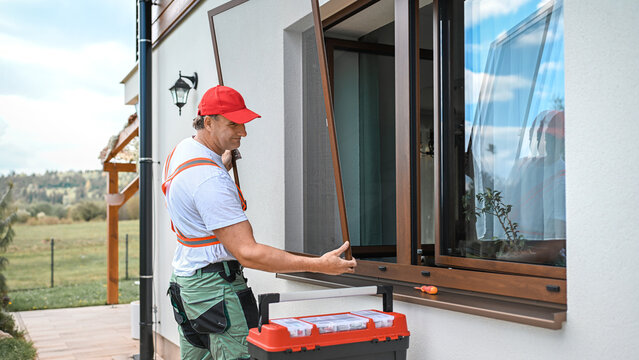 Worker installing mosquito wire screen on house window to protect from insects.