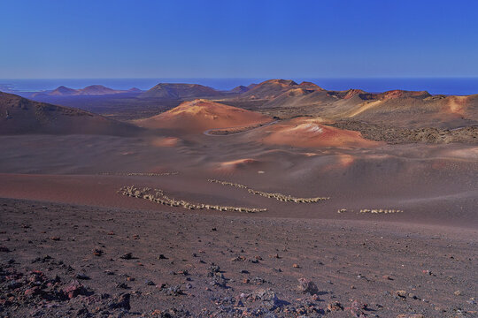 View of the volcanic landscape of Timanfaya National Park with dark lava fields, red craters, and clear blue sky in Lanzarote, Canarias, Spain.