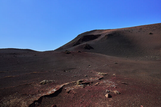 View of the volcanic landscape with red and black soil and rocky terrain under a clear blue sky in Lanzarote, Canarias, Spain.