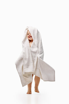 Laughing toddler girl standing wrapped into white towel. Concept of bath time fun, drying, hygiene and joyful self care, for parenting, healthcare and education.