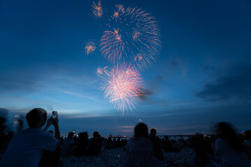 Obraz premium Fireworks bursting above spectators on an Osaka beach at dusk