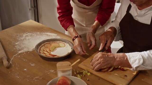 Caucasian seniors baking homemade apple pie together, slicing fruit and arranging pastry dough in pan. Clip fits culinary commercials, baking tutorials, and family lifestyle campaigns