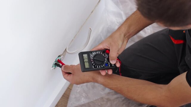 Man use a digital multimeter and probes to test the voltage of an electrical outlet.